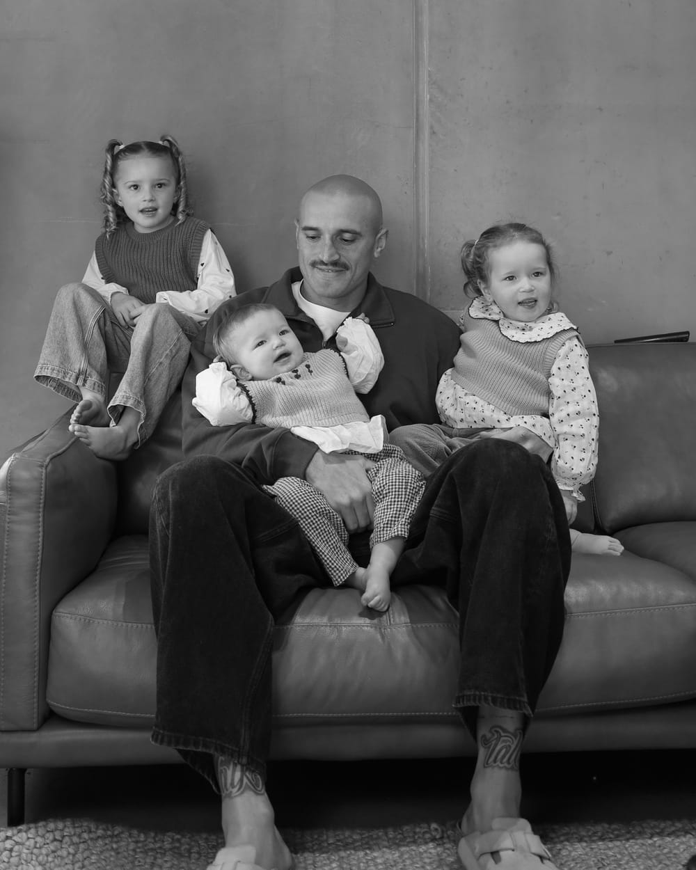 Sam Powell-Pepper at home on a couch with his three daughters.