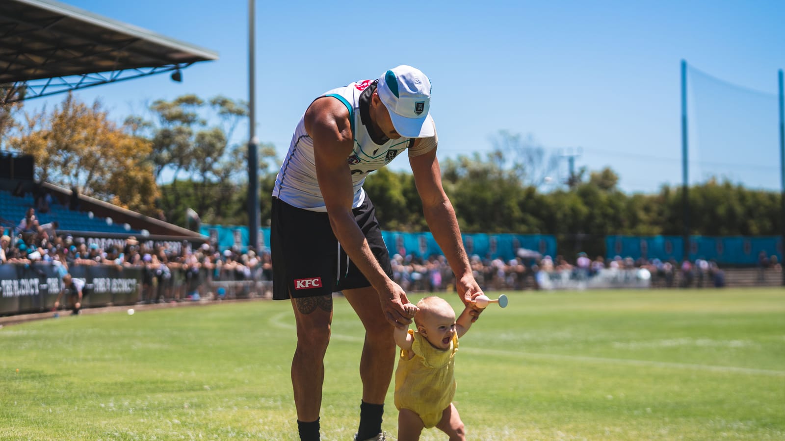 Sam Powell-Pepper crouching to hold his young daughter's hands on the field after training.