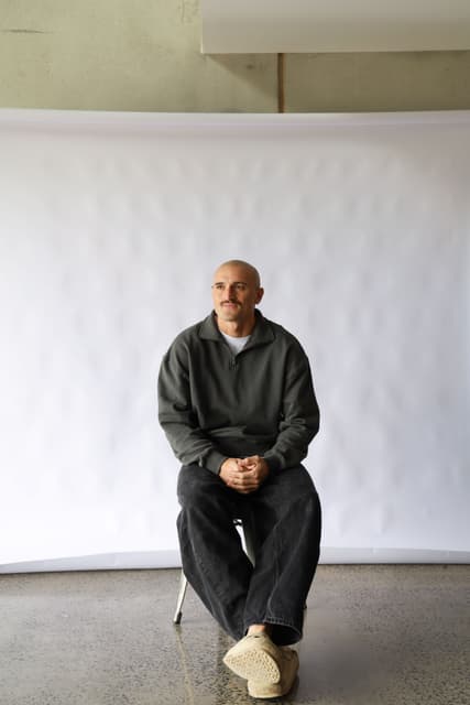 Sam Powell-Pepper seated in front of a white studio backdrop.