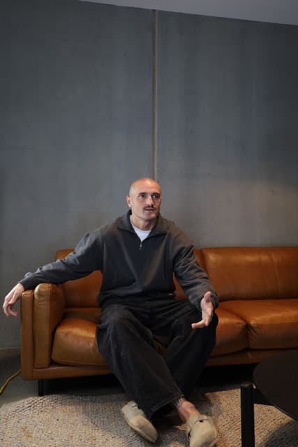 Sam Powell-Pepper on a leather couch with his hands open, talking.