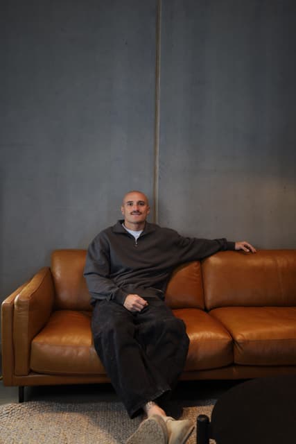 Sam Powell-Pepper sitting back on a leather couch.